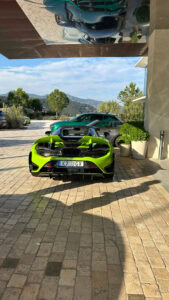 Luxury green sports car parked outside the Maybourne Riviera hotel in Monaco with scenic mountain view.