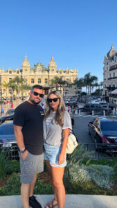 Elegant couple sightseeing in Monaco with historic casino building in background.