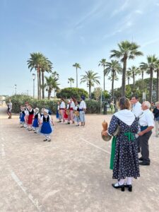 Colorful traditional folk dancers in historic costumes performing outdoors beneath palm trees in a sunny seaside promenade in Antibes, France.