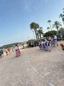 Colorful traditional dancers performing on a sandy beach promenade with palm trees under a clear blue sky in Antibes, France.