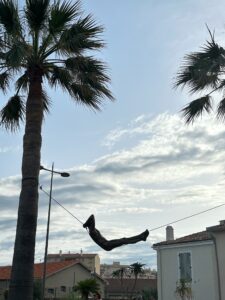 Modern art statue on a street cord with palm trees and residential buildings in the background in Antibes, France.