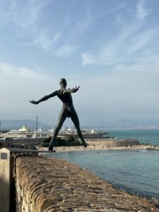 Modern sculpture of a dancer by the waterfront with yachts and scenic coast in the background in Antibes, France.