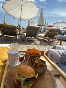 Beachside lunch with burger, fries, and sweet potato wedges under umbrellas in Cannes, France.