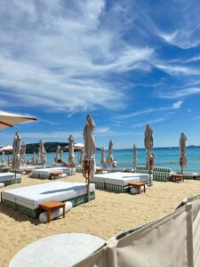 Bright beach umbrellas and loungers on sandy shore with clear blue sky and ocean backdrop in Saint Tropez, France.