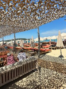 Shaded beach lounge area with umbrellas, sunbeds, and people enjoying a seaside vacation.