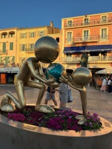 Metal sculptures of people holding globes in a lively city square in Saint Tropez, France.