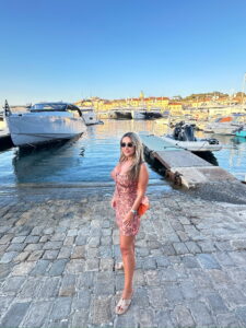 Elegant woman in pink dress standing by a luxury marina with boats and yachts.