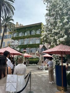 Charming outdoor Dior Restaurant cafe with pink umbrellas, lush greenery, and vintage buildings in a stylish European setting in Saint Tropez, France.