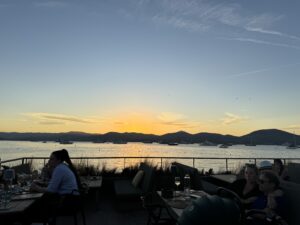 Sunset over waterfront dining with yachts in the background, scenic harbor views, and people relaxing.