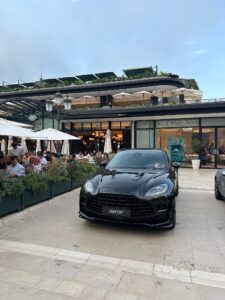 Black luxury sports car parked in front of Tiffany & Co. stores and outdoor dining areas in Monte Carlo Monaco.
