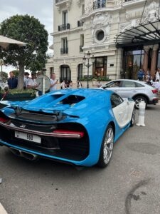 Blue Bugatti Chiron parked outside luxury Hotel de Paris with people admiring the car.