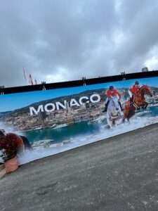 Colorful Monaco travel poster with horseback riders by the waterfront.