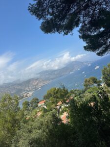 Scenic coastal view with boats, mountains, and lush greenery in a sunny harbor area.