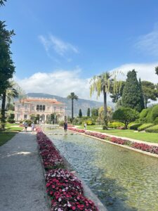 Colorful garden with pink flowers, fountain, and grand mansion under sunny sky in a luxurious estate. Villa Ephrussi de Rothschild in Saint Jean Cap Farrat