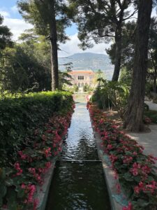 Luxurious mansion overlooking mountain with garden and flower-lined water fountain pathway. Villa Ephrussi de Rothschild in Saint Jean Cap Farrat