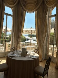 Elegant dining area with large windows and luxurious drapery overlooking a terrace with umbrellas.