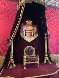 Ornate throne with royal crest and velvet drapes in the historic Prince's Palace in Monaco.