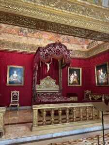Luxurious ornate royal bedroom with red velvet decor and gold accents in Prince's Palace in Monaco.