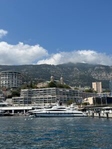 Luxurious yacht docked in Monaco harbor with Monte Carlo skyline and mountains in background, scenic Mediterranean view.