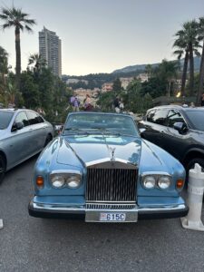 Vintage Rolls Royce car parked in Monaco with cityscape and palm trees background.