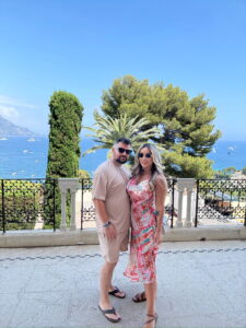Beautiful couple enjoying a Mediterranean seaside view with lush greenery and blue waters.