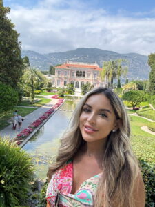 Elegant woman with long blonde hair at luxurious botanical garden, scenic palace villa backdrop.