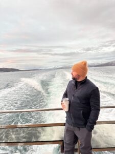 Man on boat holding insulated tumbler with scenic fjord view in background in Norway