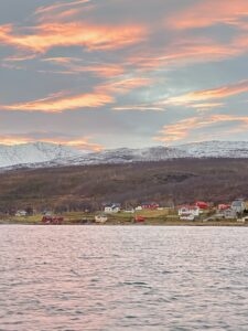 Colorful sunset over coastal village with mountains and water in background in Norway.
